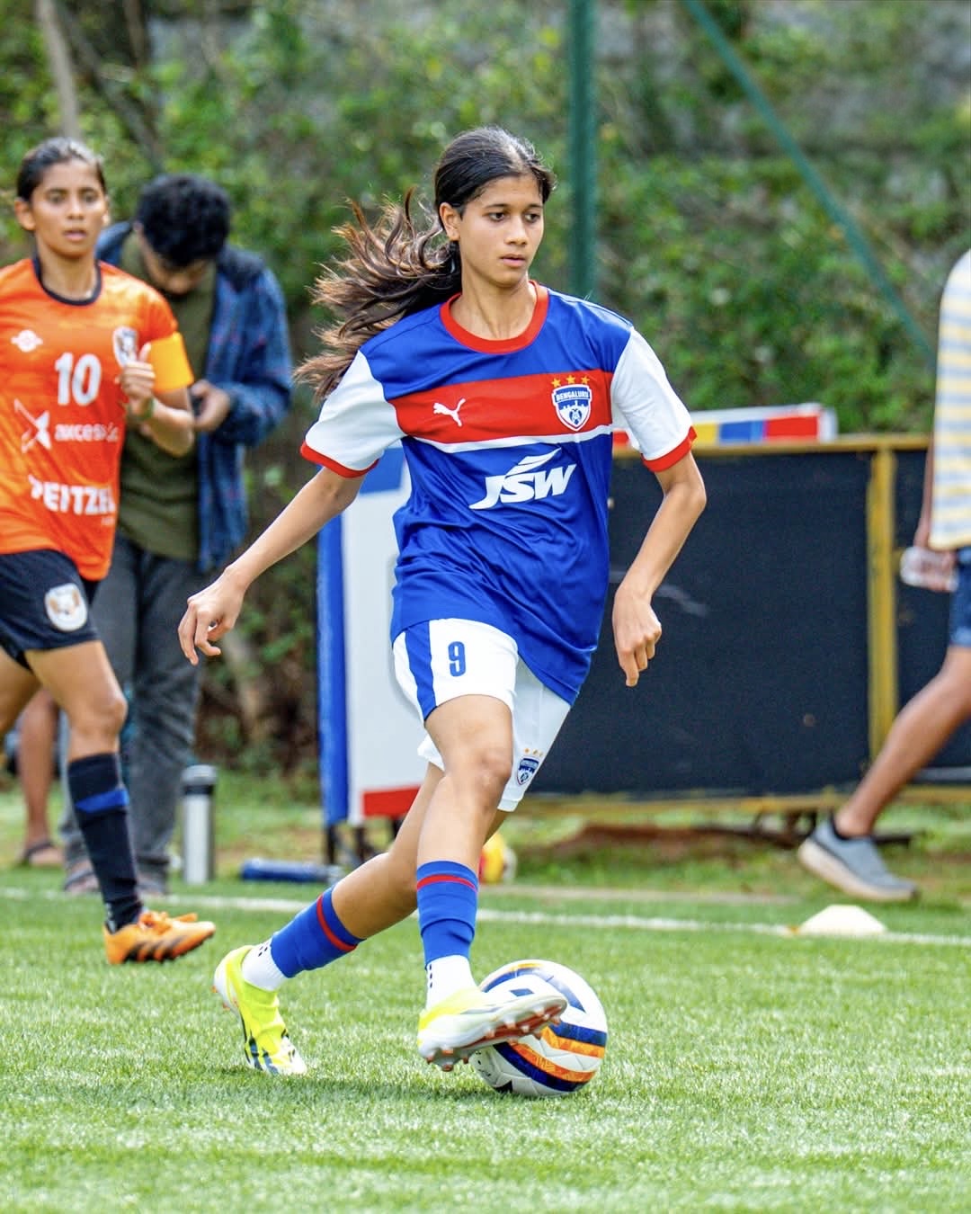 Tanvi Nair dribbling a football in her blue, red and white Bengaluru FC number 9 jersey