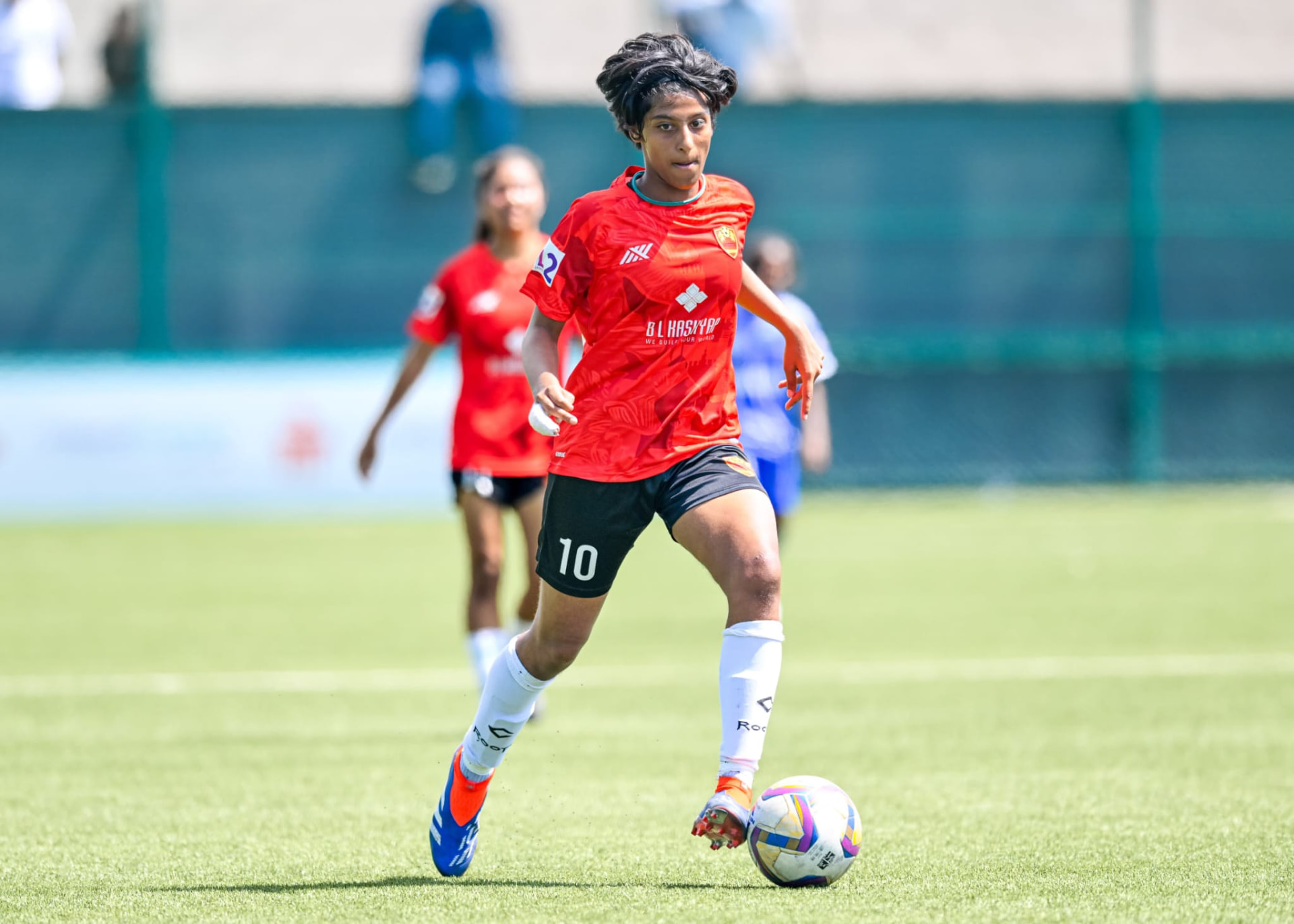 Maithreyi running with a football in her red jersey and number 10 shorts